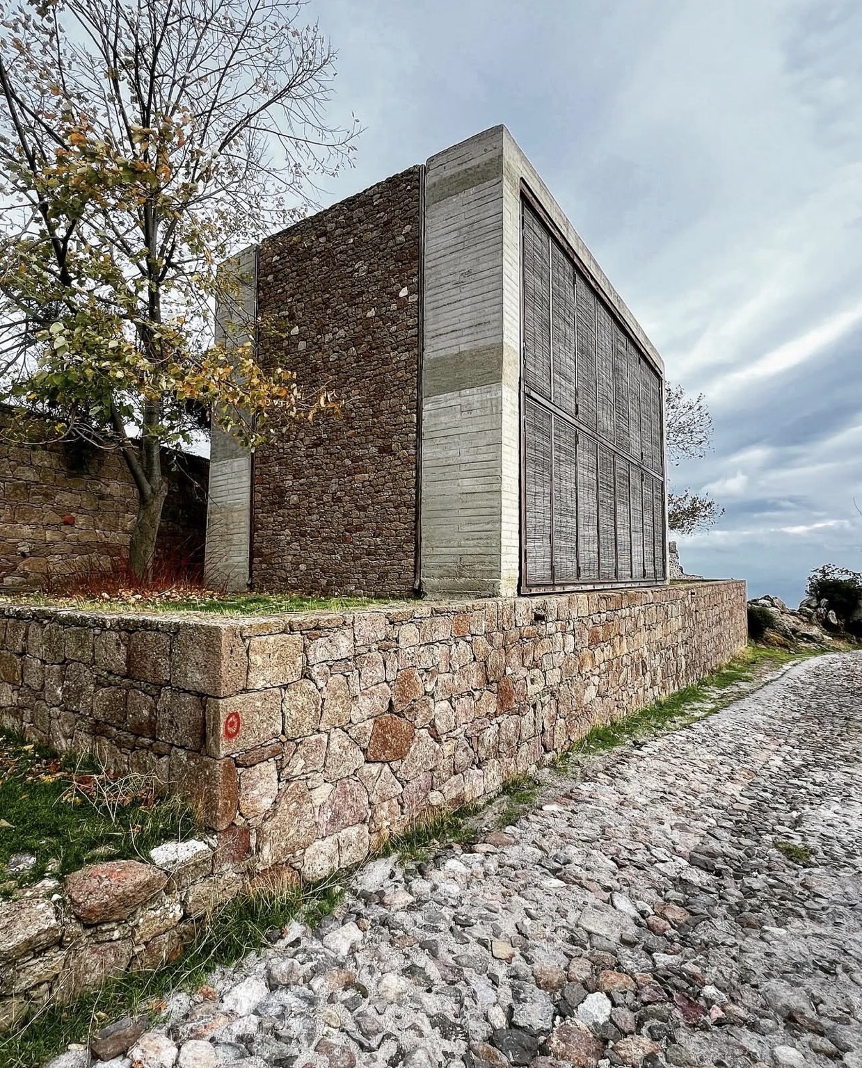 Stone and exposed-concrete exterior of B2 House beside a cobbled village road