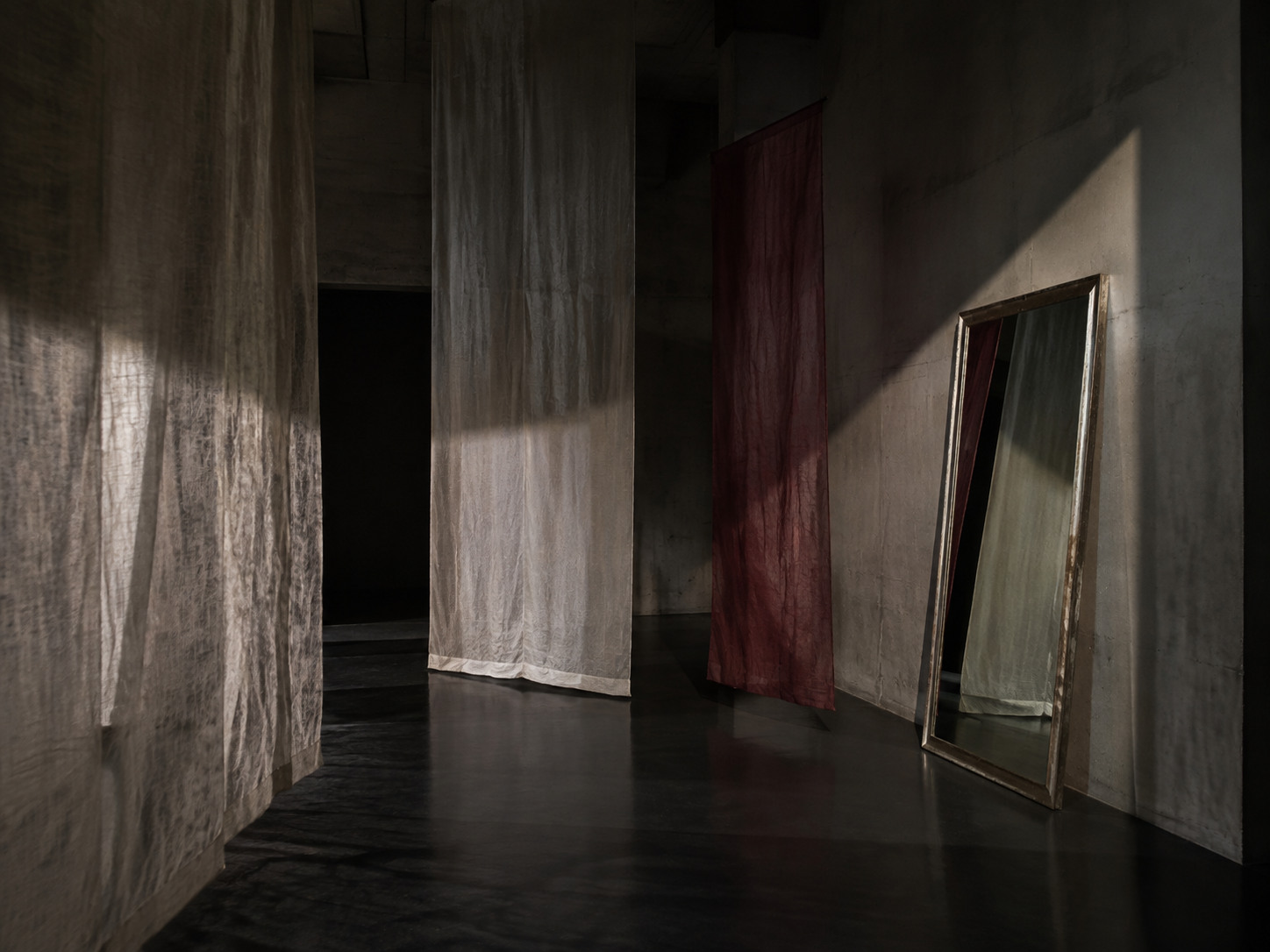 An original dark gallery installation of suspended cloth, mirror and shadow