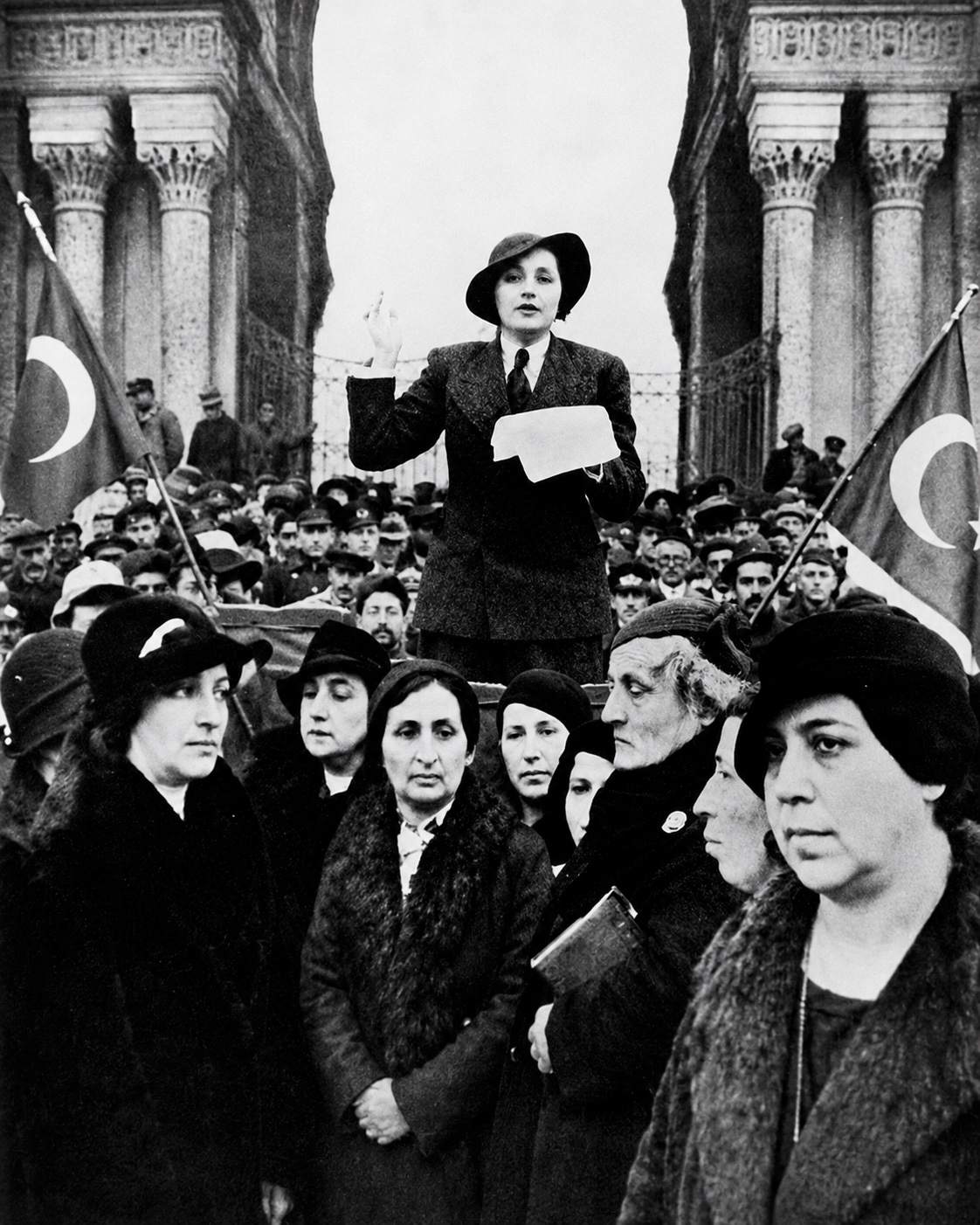 A woman addresses a crowd gathered with Turkish flags in an archival photograph