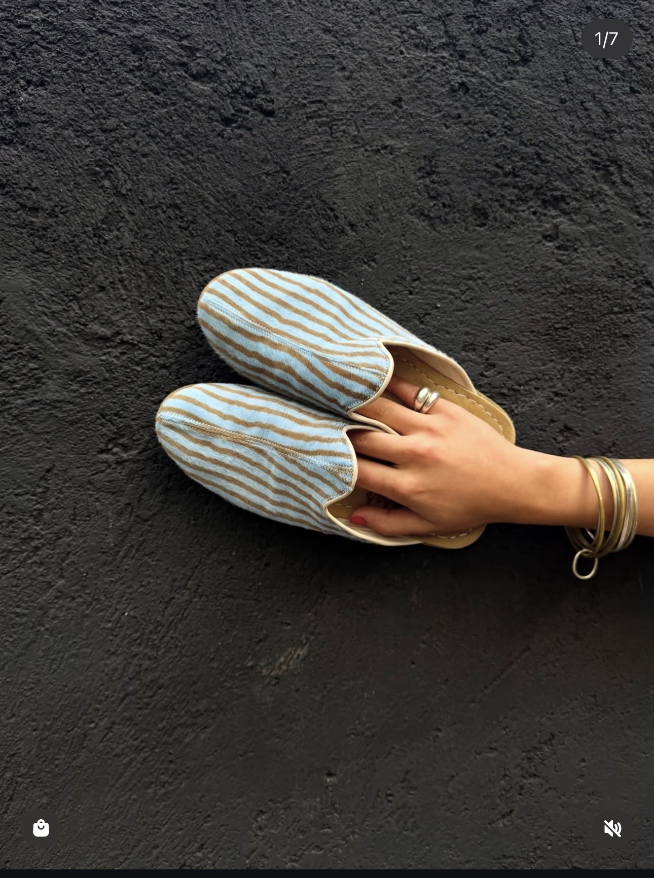 Striped backless yemeni slippers held against a black wall