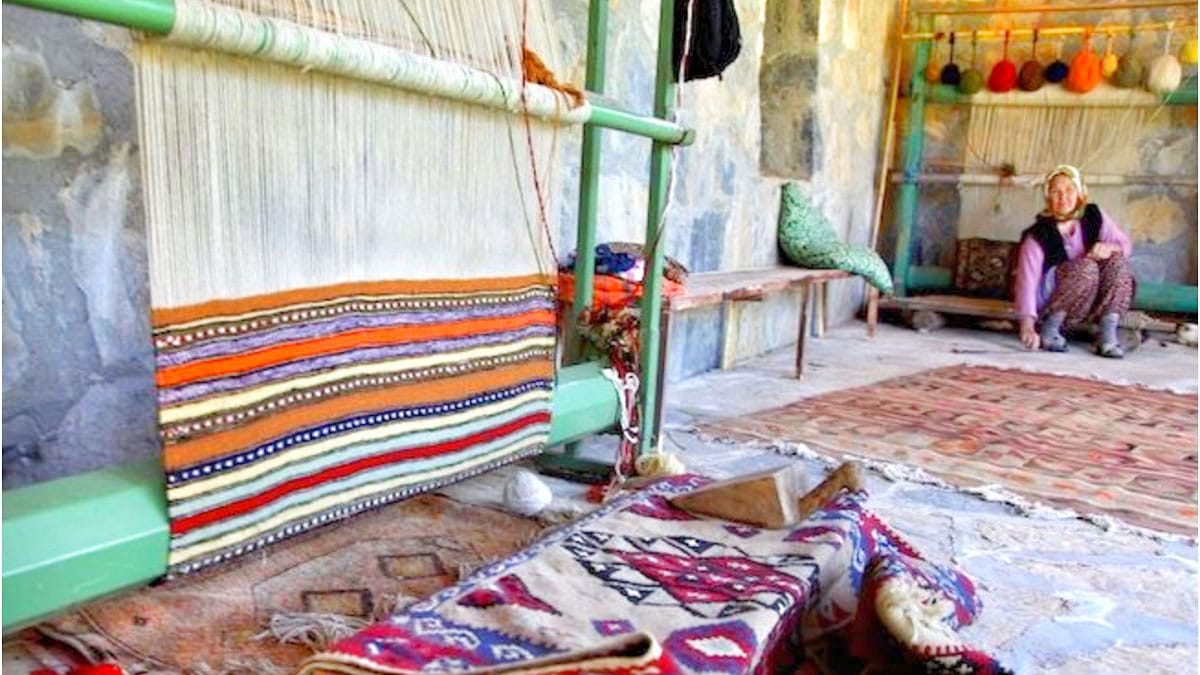 A weaver seated beside carpets and a loom in Etrim Village